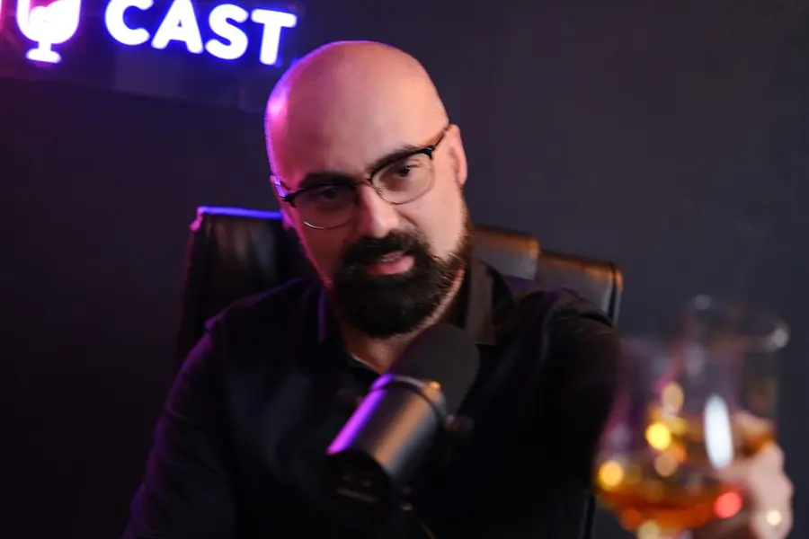 Apresentador brindando no Estúdio Mesacast, com letreiro em neon ao fundo